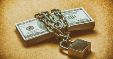 A stack of cash money is locked up with chains and a padlock.