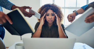 A frustrated woman looks into the camera while surrounded by the hands of various people trying to get her attention.